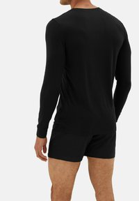 Sort langærmet skjorte med rund hals, lavet af blødt stof. Bæres med matchende sorte shorts, der viser et slim fit design.