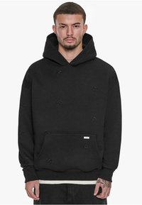 Schwarzer Kapuzenpullover aus weichem Stoff mit einer großen Kapuze, einer Fronttasche und dezenten geprägten Logomustern überall. Mit gerippten Bündchen und Saum.
