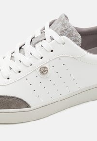 Bílé kožené tenisky s šedým semišovým špičkou a vzorovaným šedým textilním límcem. Obsahuje bílé šňůrky a malé boční perforace. Stříbrný akcent s logem.