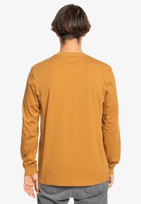 Long-sleeve shirt in mustard yellow, made of soft fabric. Features a round neck and straight cut; minimal stitching and no visible patterns.