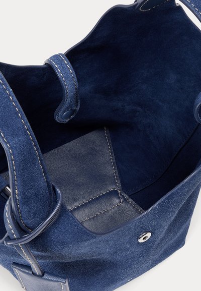 Navyblå mockaväska med en mjuk textur, utrustad med ett läderfoder, stadiga handtag och ett knappstängning. Insidan har en slät yta.