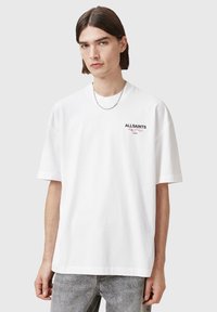 White cotton t-shirt with a relaxed fit, short sleeves, and a crew neck. Features a small black and red logo on the chest.