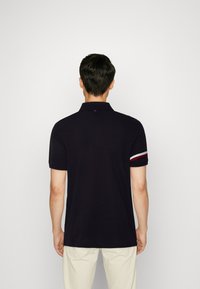 Námořnická modrá polo košile s límcem, krátké rukávy a barevně kombinované akcenty v červené a bílé na manžetách.