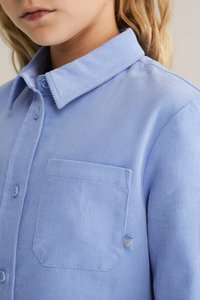 Camasa din culori albastre deschise din catifea cu nasturi, cu guler, având un buzunar pe piept și o textură subtilă ribbed verticală.