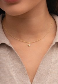 Collana in oro con pendente a forma di stella che presenta un gemma trasparente centrale. La catena ha un design delicato e strutturato.
