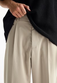 Maglione a coste nero che copre parzialmente pantaloni beige plissettati. Il tessuto sembra liscio con dettagli di cucitura visibili sui pantaloni.