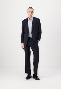 Marineblauwe dubbelbreasted colbert met notch revers, gecombineerd met een lichtblauw overhemd en op maat gemaakte broek, aangevuld met zwarte veterschoenen.