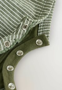 Zeleno prugasta tkanina z metalnimi pritisnimi gumbi ob ovratniku; združuje teksturiran zeleni material z svetlejšo prugasto zasnovo.