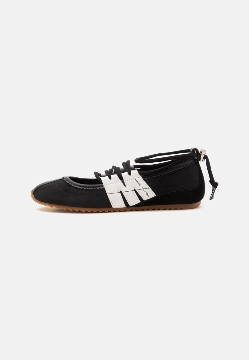 Chaussure plate noire avec des bandes de logo blanches cousues, des lacets élastiques et une semelle marron rainurée, avec une fermeture à cordon au talon.
