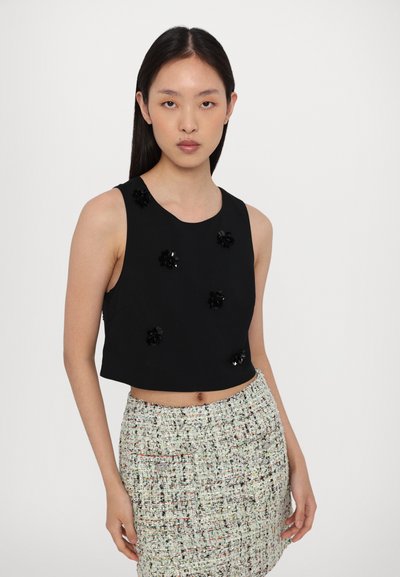 Black cropped tank top with decorative black floral appliqués and a round neckline, paired with a textured multi-colored tweed skirt.