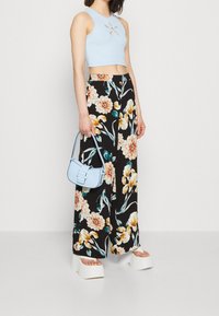 Débardeur court bleu clair avec une découpe en fleur, pantalon large à imprimé floral noir, et un petit sac à main bleu clair. Sandales compensées.