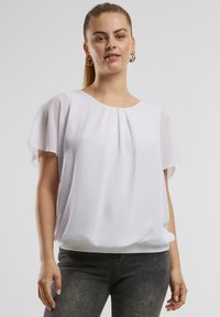 Blusa bianca con maniche corte a campana, scollatura rotonda e vestibilità ampia. Realizzata in tessuto leggero con una texture liscia.