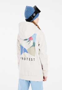 Crème hoodie met een grafisch bergontwerp in blauw, groen en roze op de achterkant, met "PROTEST" eronder gedrukt.