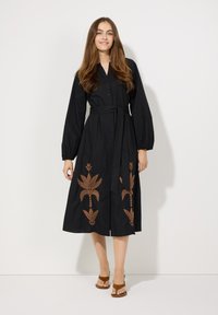 Schwarzes Hemdblusenkleid mit langen Ärmeln, versehen mit brauner Blumenstickerei und einem passenden Gürtel in der Taille. Aus leichtem Stoff gefertigt.