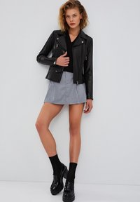 Giubbotto in pelle nera da motociclista con zip argentate, abbinato a una gonna grigia. La modella indossa scarpe con plateau nere e calze sopra il ginocchio.
