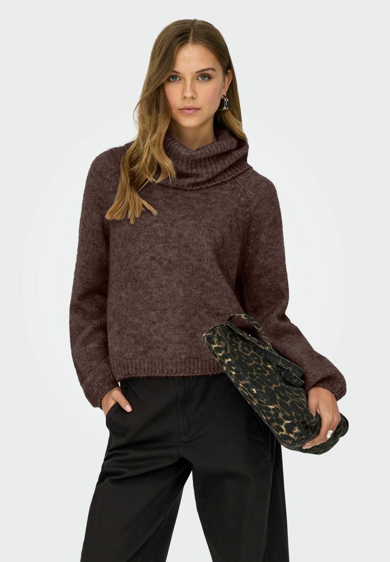 Brūna cowl-kakla džemperis ar teksturētu apdari un ribotu apakšdaļu, apvienots ar leopardu raksta somu. Modelis valkā melnas bikses.