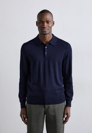Navyblauw long-sleeve polo shirt van zacht materiaal, met een kraag en een drieknoopssluiting, gecombineerd met gestructureerde groene broek.