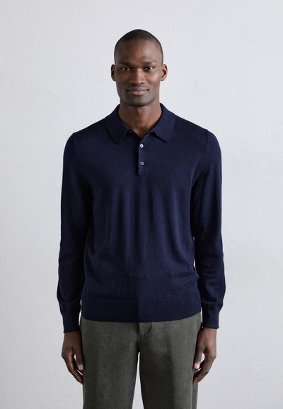 Navyblauw long-sleeve polo shirt van zacht materiaal, met een kraag en een drieknoopssluiting, gecombineerd met gestructureerde groene broek.