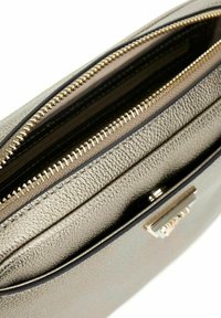 Sac en imitation cuir doré métallique avec une ouverture zippée et une surface texturée. Présente un accent de marque subtil et un intérieur contrasté.