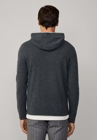 Maglione grigio con cappuccio, dalla consistenza morbida, design aderente e polsini a coste. Vista dal retro, indossato sopra una maglietta bianca.