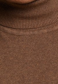 Nahaufnahme eines braunen gerippten Rollkragens auf dem Hals einer Person, die die Strickstruktur und die Stoffdetails zeigt.