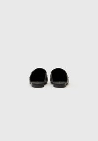 Black leather slip-on shoes with a flat sole, rounded back, and minimal detailing. Smooth texture and open design at the heel.