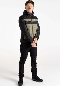 Gepolsterte Jacke in Schwarz und Olivgrün mit einem Reißverschluss vorne, Kapuze und elastischen Bündchen. Getragen mit schwarzen Hosen und robusten schwarzen Stiefeln.