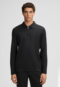 Czarna longsleeve polo z zamkiem przy kołnierzyku. Wykonana z gładkiego materiału, z luźnym krojem i minimalistycznym wzornictwem.