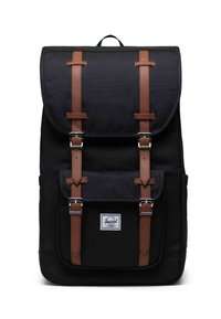 Schwarzer Stoff-Rucksack mit einem Klappenverschluss, braunen Lederträgern, Metallbeschlägen, einer Fronttasche und einem weißen Markenetikett.