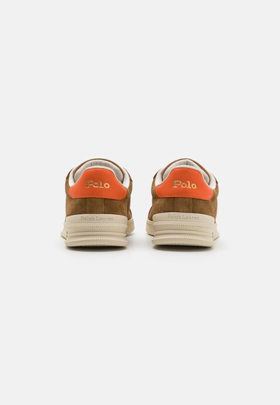 Adidași din suede de culoare tan cu accente portocalii pe călcâi și talpă bej. Logo-ul "Polo" embosat pe călcâi și limbă. Textură netedă și formă rotundă.