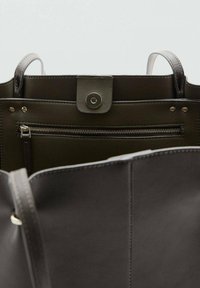 Bolso de cuero verde oscuro con parte superior abierta, que cuenta con un bolsillo interior con cremallera y cierre a presión. Asas planas acopladas para facilitar el transporte.