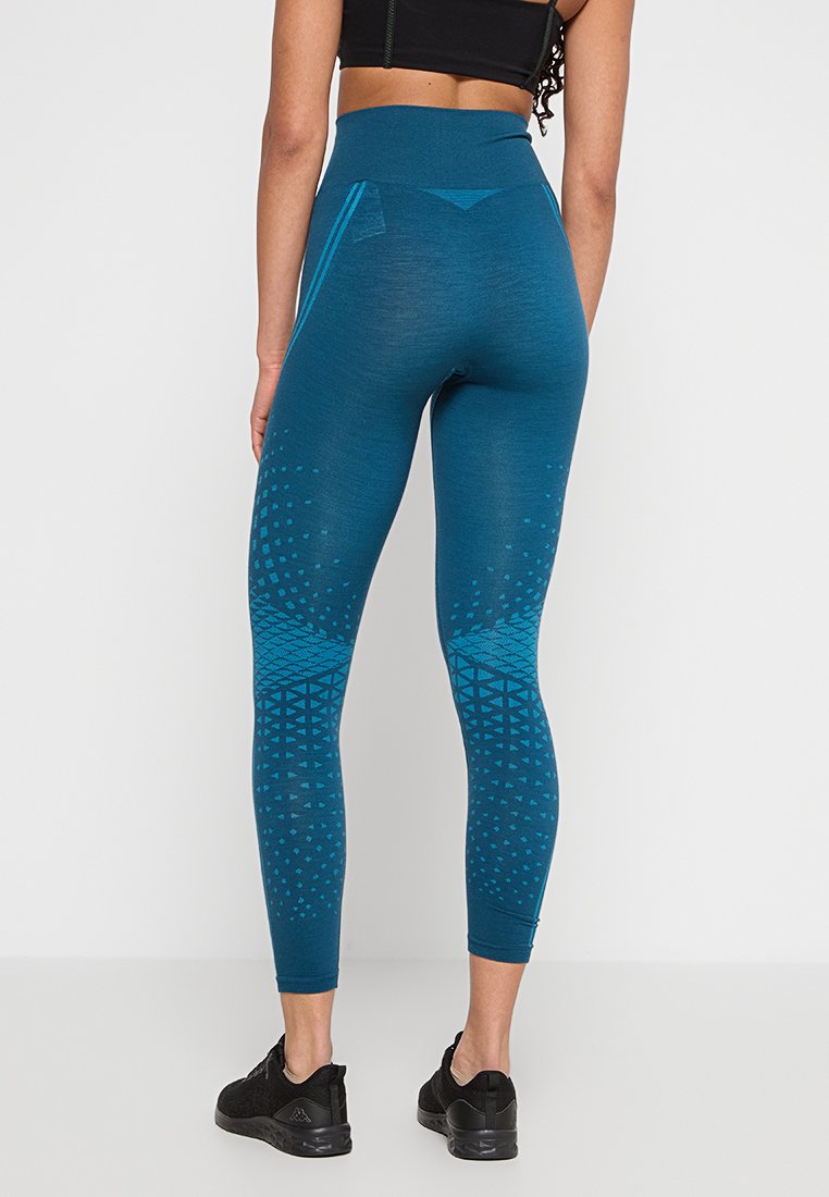 Turkusowe legginsy fitness z wysokim pasem. Teksturalne geometryczne wzory w ciemniejszych odcieniach, gładki materiał i dopasowany krój. Czarne obuwie.