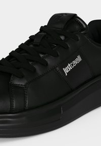 Μαύρο sneaker χαμηλής κοπής με μαύρα κορδόνια, επάνω μέρος από δέρμα, χοντρή σόλα και λευκό λογότυπο Just Cavalli στην πλευρική επιφάνεια.