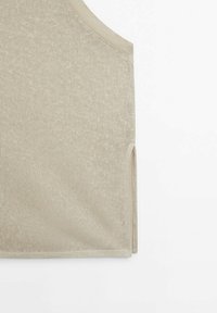 Haut sans manches beige en maille avec fente latérale sur fond blanc.