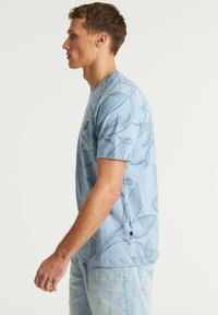 Šviesiai mėlyna marškinėliai su botanikos raštu tamsesnėje mėlynoje spalvoje, apvaliu kaklu, trumpomis rankovėmis ir šonine etikete.