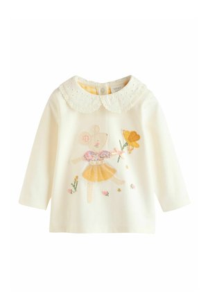 Valge pikkade varrukatega särk pitskraega. Ees on tikitud karu kollases kleidis, kes hoiab lille, teda ümbritsevad väikesed lillemustrid.