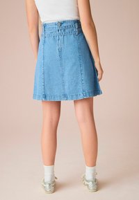 Leren rok in lichtblauw met een aansluitende tailleband, rits in het midden en A-lijn vorm. Heeft een onafgewerkte zoom. G gedragen met zilveren sneakers.