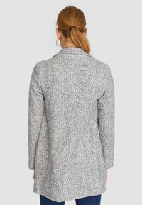 Grauer Mantel mit strukturierter Oberfläche und tailliertem Schnitt, mit langen Ärmeln und einem Reverskragen, von der Rückseite gezeigt.