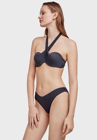 Tamno siva bikini koji se sastoji od halter kroja s teksturom i detaljem čvora, te uparene gaće s niskim strukom, naglašava glatku prilagodbu i minimalistički dizajn.
