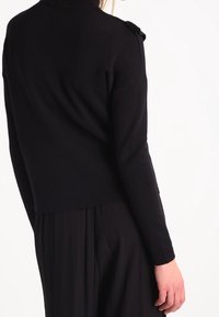 Svart stickad tröja med halvkrage och axeldetaljer. Designen har en figursydd form och långa ärmar.