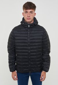 Giacca nera imbottita con cappuccio, caratterizzata da un design trapuntato orizzontale, chiusura frontale con zip e tasche laterali. Sembra leggera e liscia.