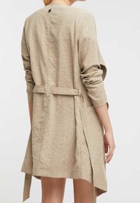 Abito wrap in lino beige chiaro con maniche lunghe, una cravatta posteriore e una linea dell'orlo dritta. Presenta un collo rotondo e una vestibilità rilassata.