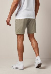 Pantaloncini color oliva chiaro fino al ginocchio, realizzati in tessuto morbido, abbinati a sneakers bianche alte. I pantaloncini presentano un taglio morbido e un orlo pulito.