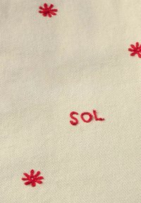 Bežna tkanina s crvenim izvezenim cvjetovima i natpisom "SOL" u ležernom, ručno pisanom stilu blizu centra.
