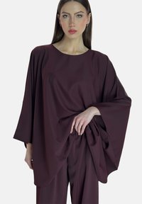 Weinrotes Batwing-Oberteil mit rundem Ausschnitt, weichem Stoff und drapierten Seiten, kombiniert mit passenden, lockeren Hosen. Glatte Textur und entspannte Passform.