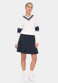 Pullover alb cu dungi bleumarin, de tip V, asortat cu o fustă plisată bleumarin. Tenisi albi și șosete crem completează ținuta.