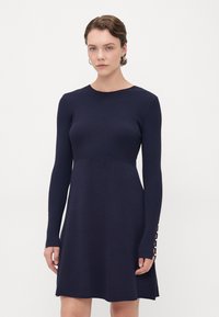Abito a maglia a coste navy con maniche lunghe, corpetto aderente, gonna svasata e dettagli in bottone sulle maniche. Texture liscia.