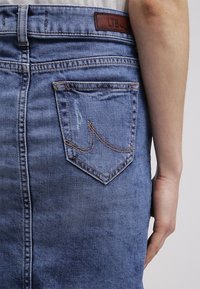 Jeanskjol i ljusblått, med en signaturstickad bakficka och lädermärke. Tyget verkar mjukt med en något sliten struktur.