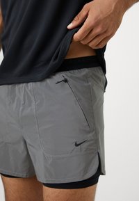 Pantalones cortos deportivos grises con una cintura elástica ajustable, bolsillo con cremallera y logo negro de Nike. Tejido que absorbe la humedad, con una textura suave.