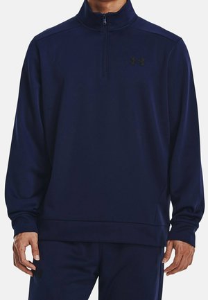 Mann trägt einen marineblauen Langarm-Quarter-Zip-Pullover mit passenden Hosen und einem kleinen Under Armour-Logo auf der Brust und dem Oberschenkel.
